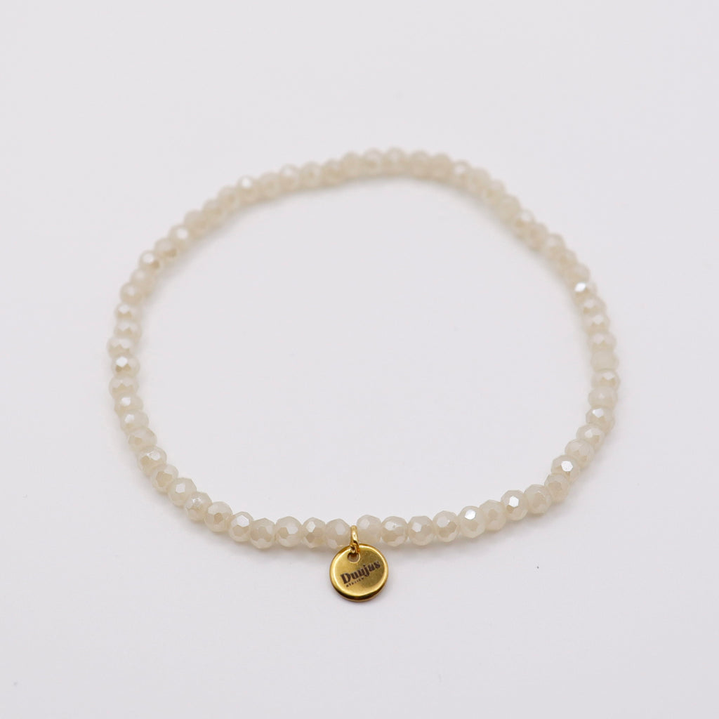 Elastisches Armband mit weissen Glasperlen und goldenem Dunjas Atelier Charm, handgemacht in Zürich
