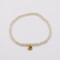 Elastisches Armband mit weissen Glasperlen und goldenem Dunjas Atelier Charm, handgemacht in Zürich