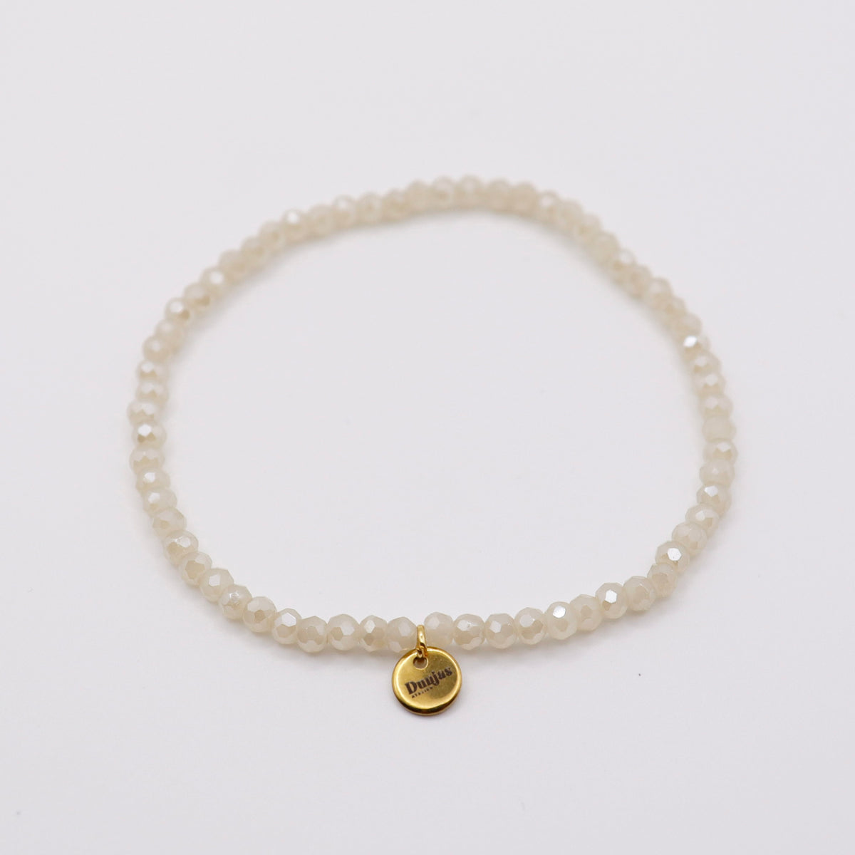 Elastisches Armband mit weissen Glasperlen und goldenem Dunjas Atelier Charm, handgemacht in Zürich