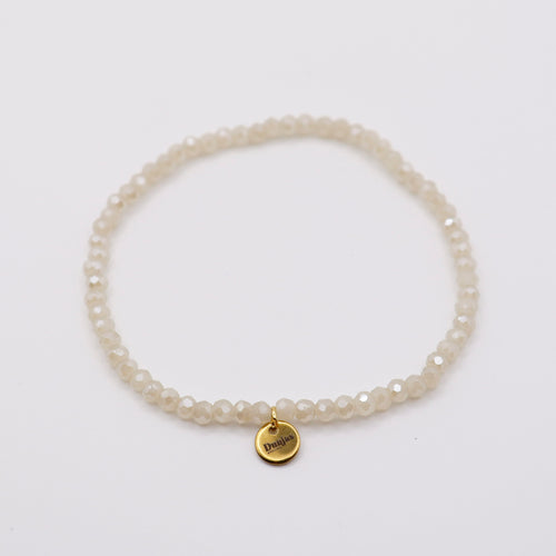 Elastisches Armband mit weissen Glasperlen und goldenem Dunjas Atelier Charm, handgemacht in Zürich