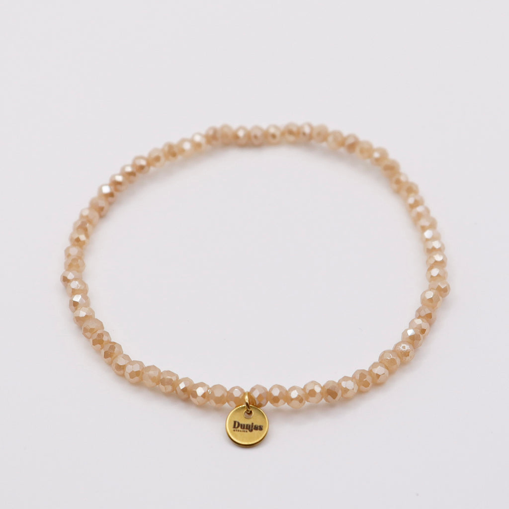Elastisches Armband mit beige-orangen Glasperlen und goldenem Dunjas Atelier Charm, handgemacht in Zürich