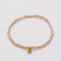Elastisches Armband mit beige-orangen Glasperlen und goldenem Dunjas Atelier Charm, handgemacht in Zürich