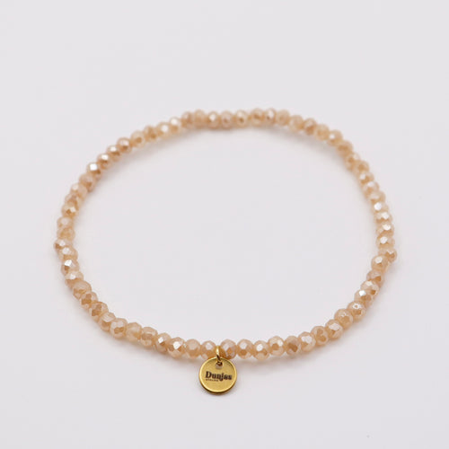Elastisches Armband mit beige-orangen Glasperlen und goldenem Dunjas Atelier Charm, handgemacht in Zürich
