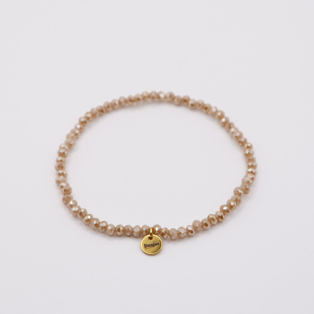 Elastisches Armband mit beigen Glasperlen und goldenem Dunjas Atelier Charm, handgemacht in Zürich
