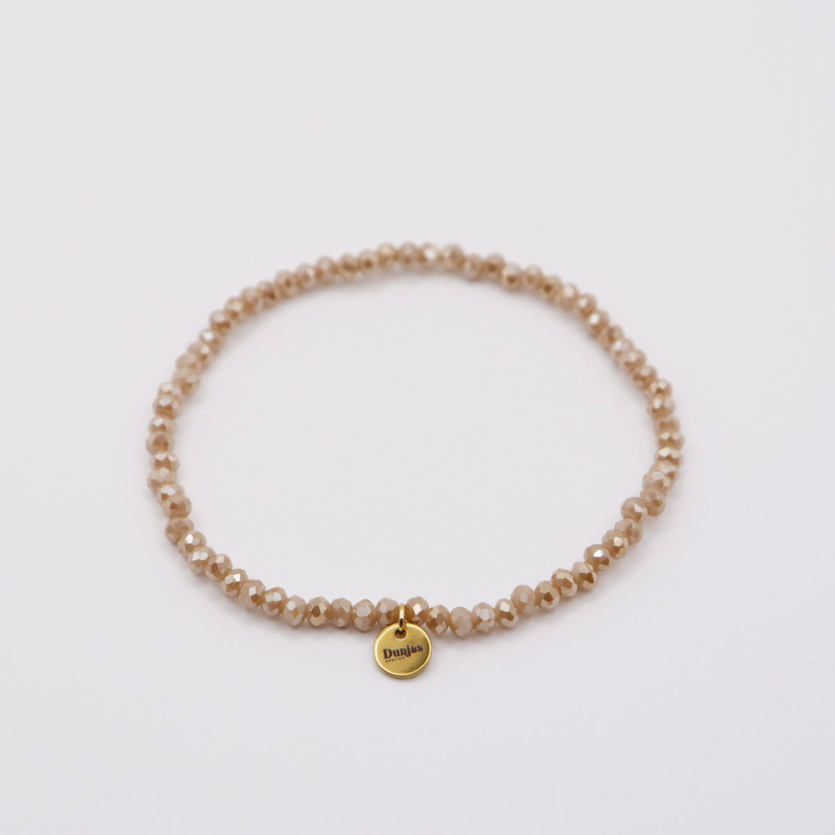 Elastisches Armband mit beigen Glasperlen und goldenem Dunjas Atelier Charm, handgemacht in Zürich