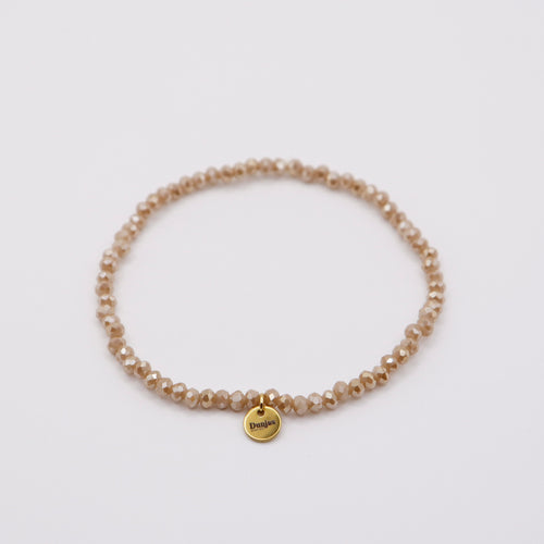 Elastisches Armband mit beigen Glasperlen und goldenem Dunjas Atelier Charm, handgemacht in Zürich