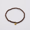Elastisches Armband mit dunkelbraunen Glasperlen und goldenem Dunjas Atelier Charm, handgemacht in Zürich